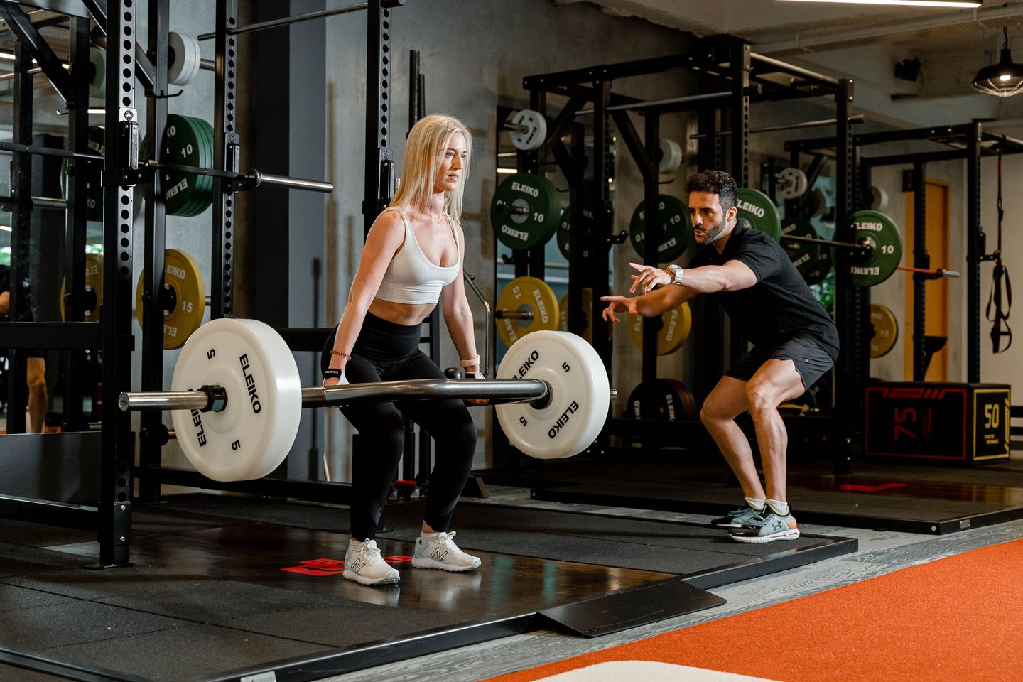 Học viên nữ tập deadlift với thanh tạ lục giác, PT quan sát kỹ thuật